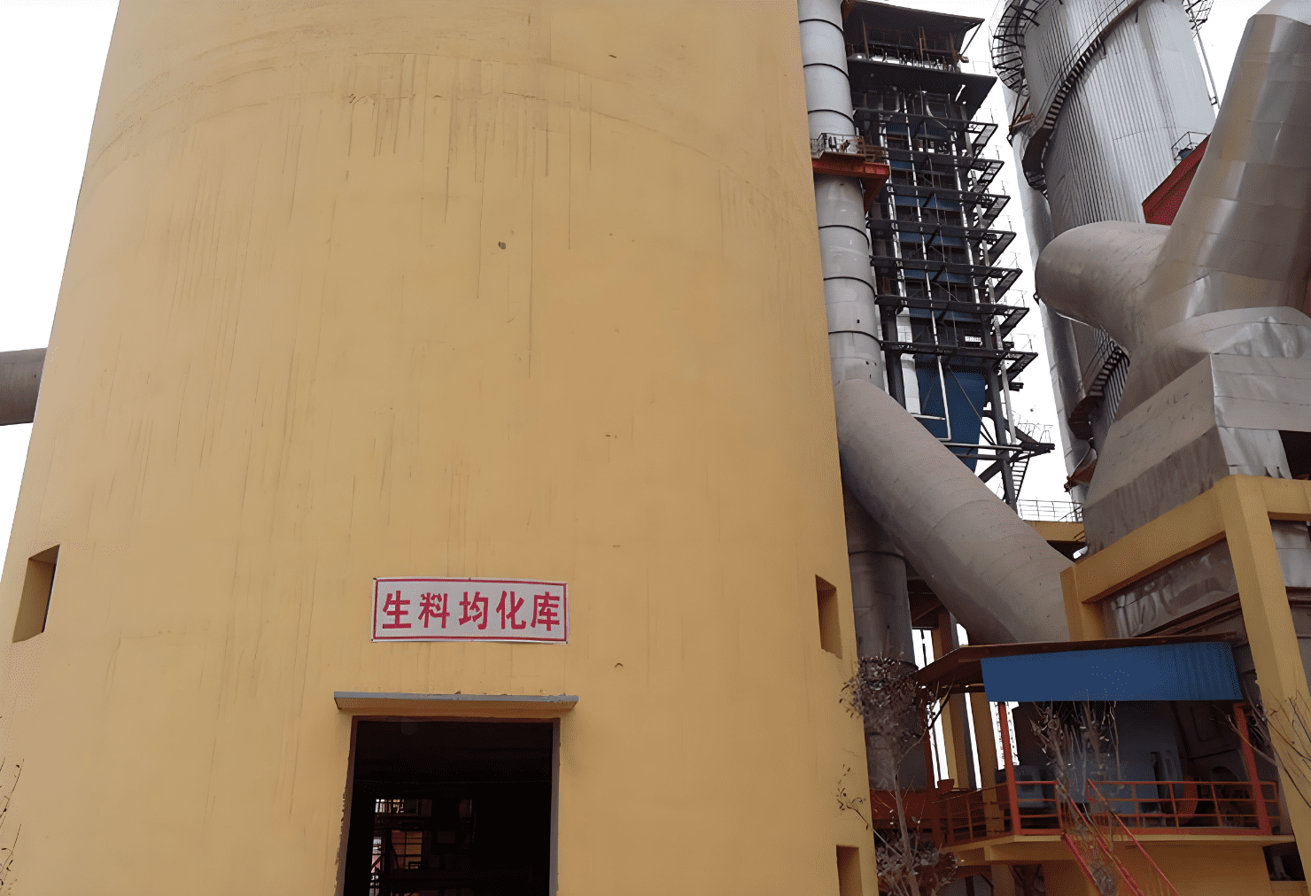 The yellow cement silo stands tall, featuring large loading ports and serving as a key storage unit in the cement production process.